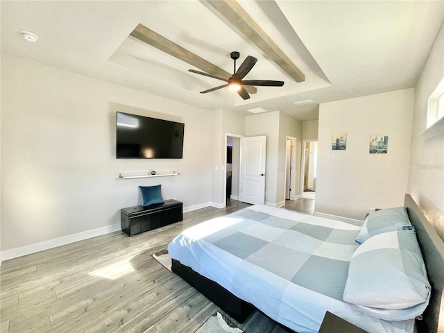 bedroom featuring a tray ceiling, wood finished floors, a ceiling fan, and baseboards