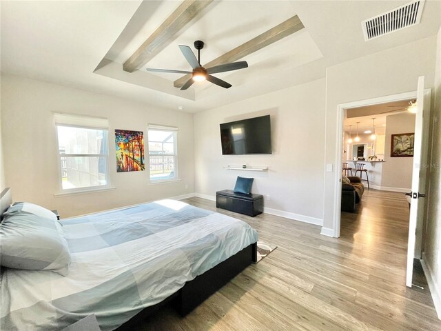 bedroom with light wood-style flooring, visible vents, a raised ceiling, and baseboards