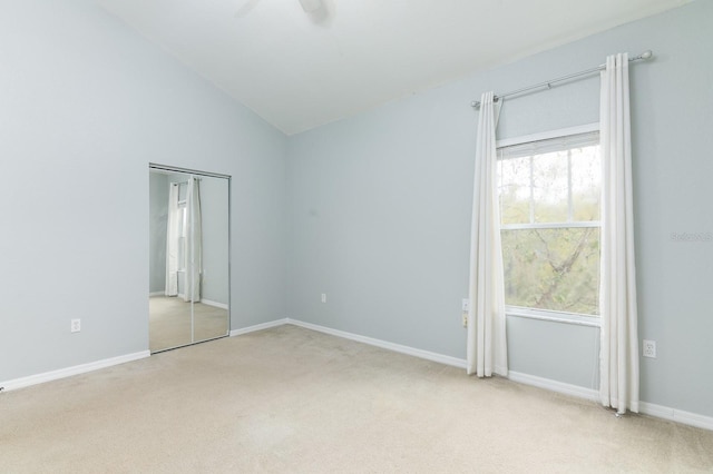 empty room with light carpet, lofted ceiling, a ceiling fan, and baseboards