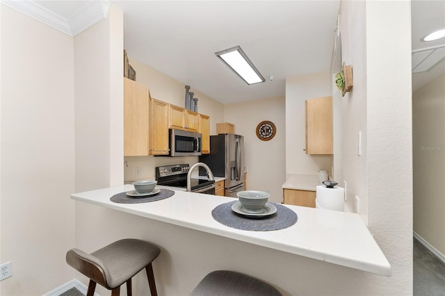 kitchen with a kitchen bar, a peninsula, appliances with stainless steel finishes, and light brown cabinetry