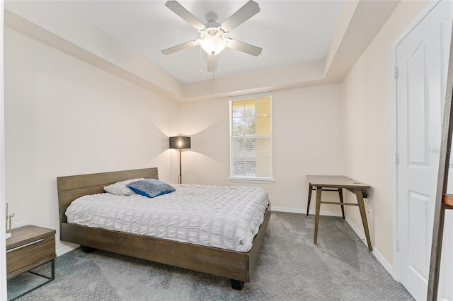 carpeted bedroom with a tray ceiling, a ceiling fan, and baseboards