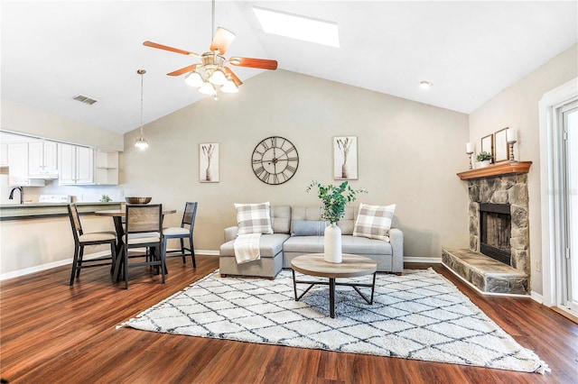 living area featuring lofted ceiling with skylight, a fireplace, dark wood finished floors, and visible vents