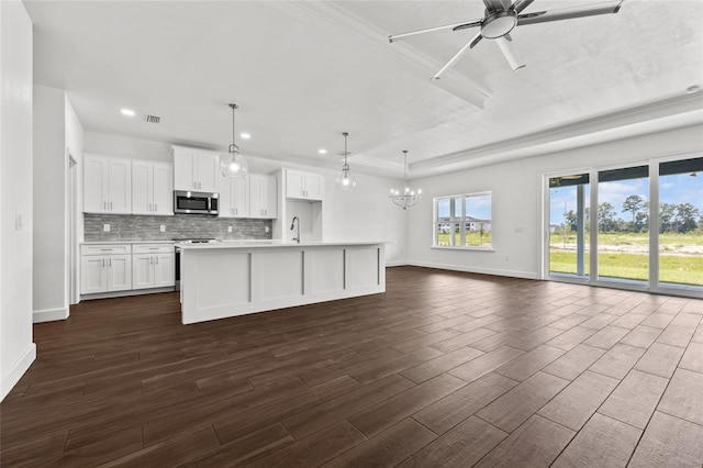 kitchen featuring a kitchen island with sink, open floor plan, light countertops, decorative backsplash, and stainless steel microwave