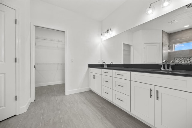 full bath with double vanity, a tile shower, a sink, and a walk in closet