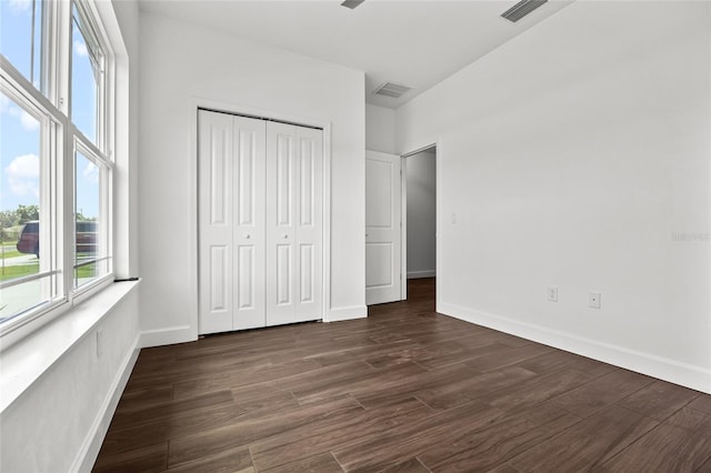 unfurnished bedroom with a closet, dark wood-style flooring, visible vents, and baseboards