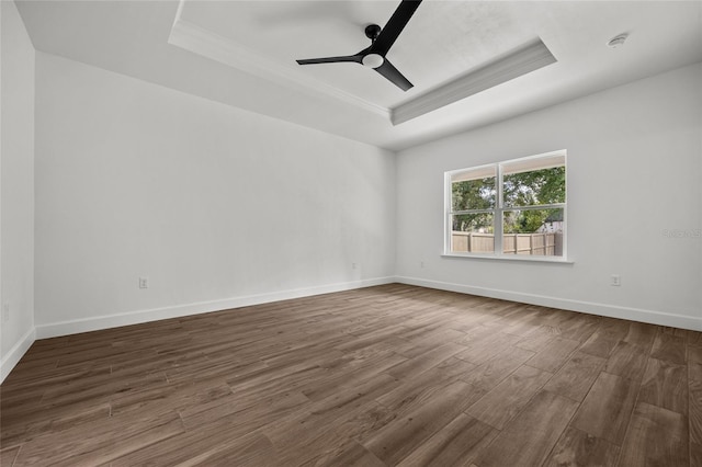 empty room with a ceiling fan, a raised ceiling, dark wood finished floors, and baseboards