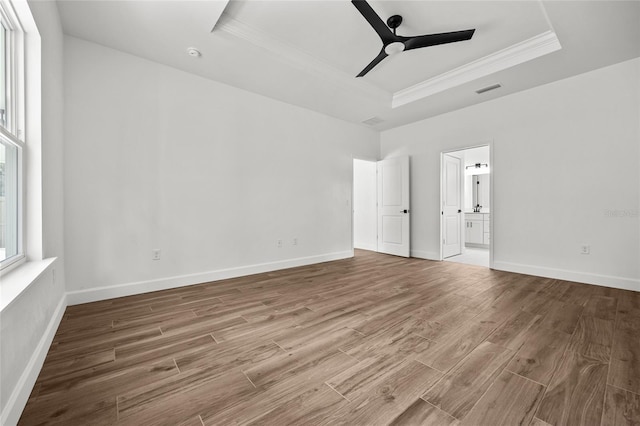 unfurnished bedroom with ensuite bathroom, a tray ceiling, wood finished floors, and baseboards