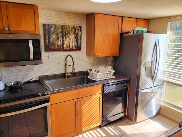 kitchen featuring appliances with stainless steel finishes, dark countertops, a sink, and backsplash