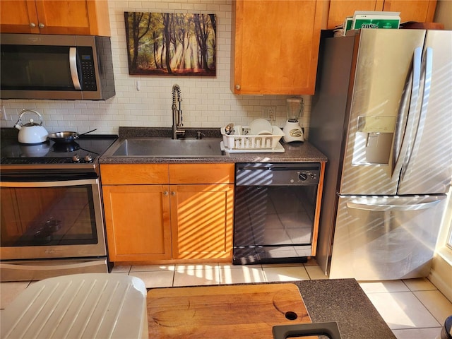 kitchen featuring light tile patterned floors, decorative backsplash, dark countertops, appliances with stainless steel finishes, and a sink