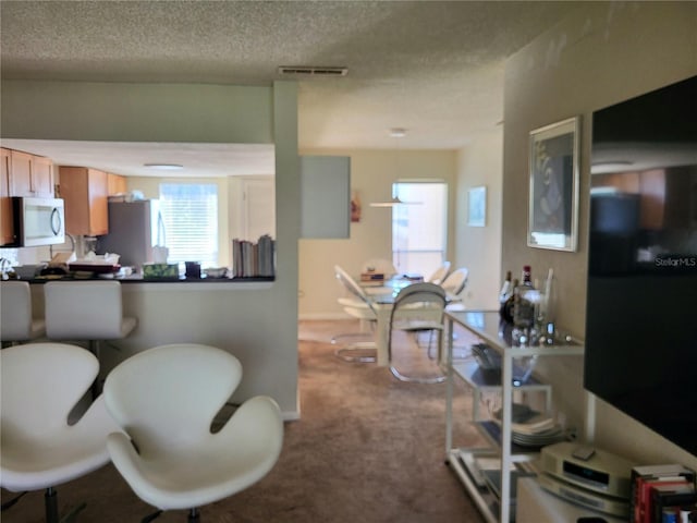 kitchen with a textured ceiling, visible vents, freestanding refrigerator, stainless steel microwave, and carpet