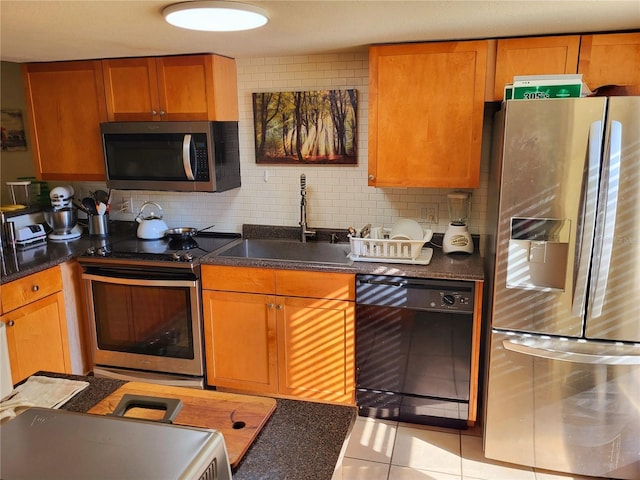 kitchen featuring appliances with stainless steel finishes, dark countertops, a sink, and tasteful backsplash