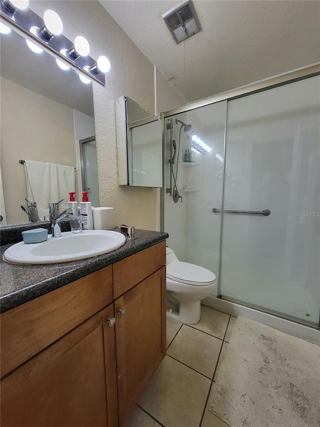 full bathroom featuring toilet, vanity, visible vents, a shower stall, and tile patterned floors