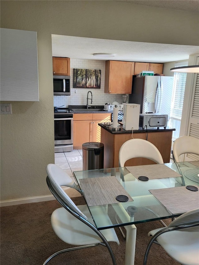 kitchen with stainless steel appliances, a sink, baseboards, backsplash, and dark countertops