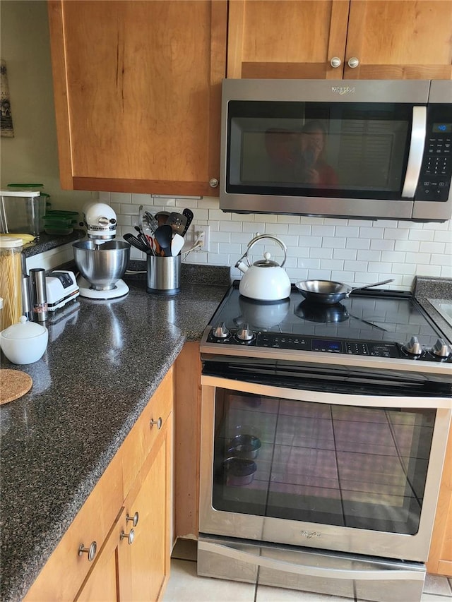 kitchen with appliances with stainless steel finishes, brown cabinets, dark stone countertops, and decorative backsplash