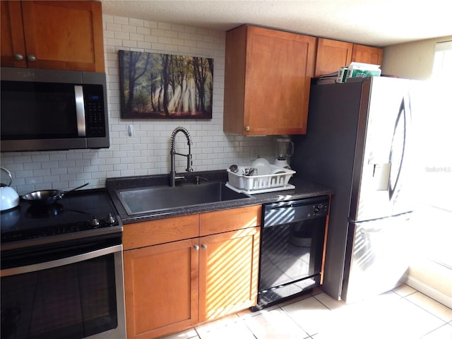 kitchen featuring stainless steel appliances, a sink, backsplash, brown cabinets, and dark countertops