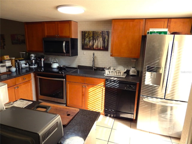 kitchen featuring dark countertops, decorative backsplash, appliances with stainless steel finishes, brown cabinetry, and a sink