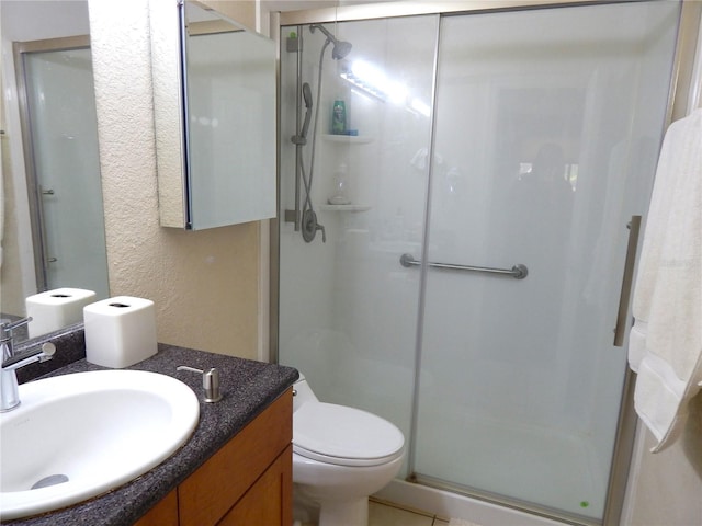 bathroom featuring a textured wall, a stall shower, vanity, and toilet