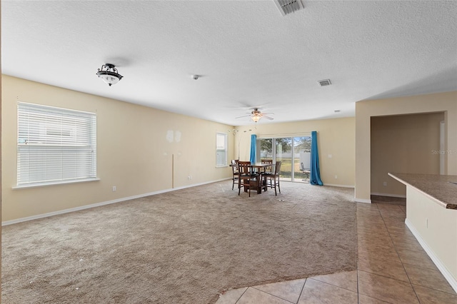 unfurnished dining area featuring light tile patterned floors, visible vents, light colored carpet, ceiling fan, and a textured ceiling