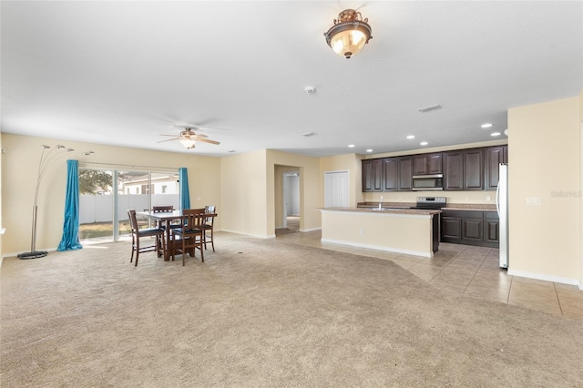 kitchen with dark brown cabinetry, a kitchen island with sink, appliances with stainless steel finishes, and light colored carpet