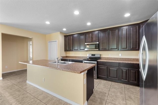 kitchen featuring an island with sink, stainless steel appliances, dark brown cabinets, a sink, and light tile patterned flooring