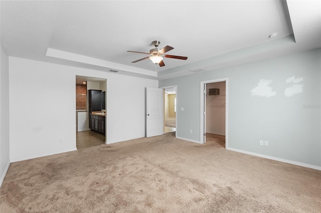 unfurnished bedroom featuring light carpet, visible vents, a spacious closet, and a tray ceiling