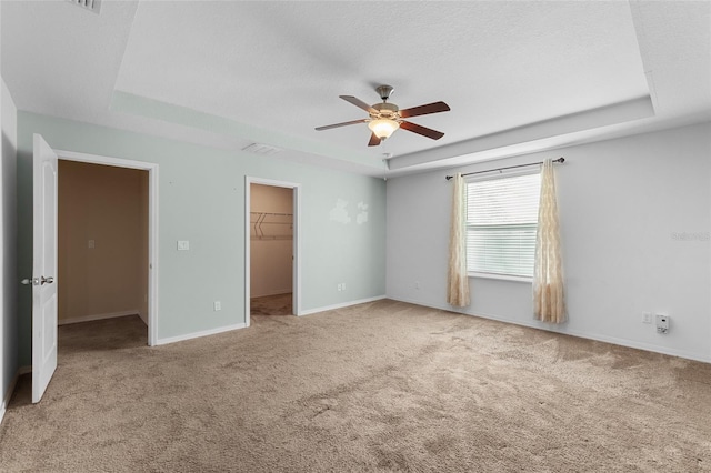 unfurnished bedroom with carpet, a raised ceiling, a spacious closet, and a textured ceiling