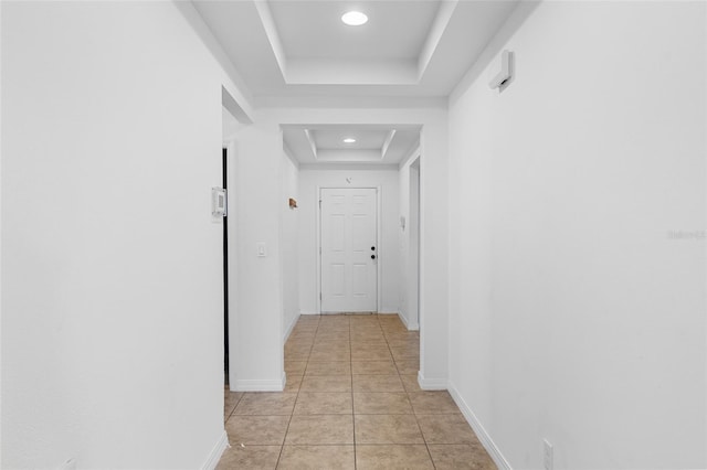 corridor with recessed lighting, light tile patterned flooring, a raised ceiling, and baseboards