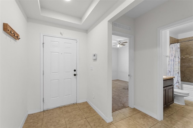 entryway featuring light tile patterned floors, a raised ceiling, visible vents, ceiling fan, and baseboards