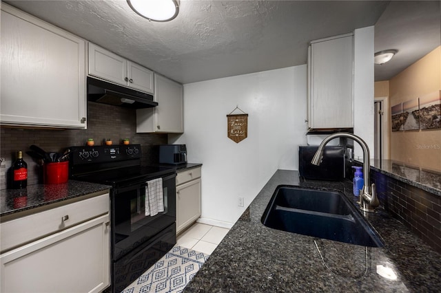 kitchen featuring backsplash, a sink, under cabinet range hood, dark stone countertops, and electric range