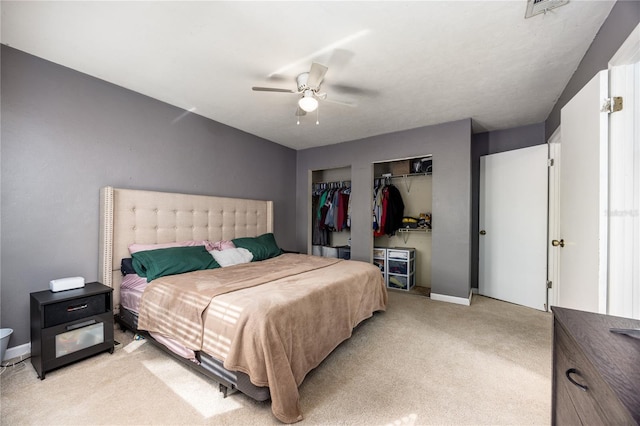 bedroom with multiple closets, visible vents, baseboards, a ceiling fan, and light colored carpet
