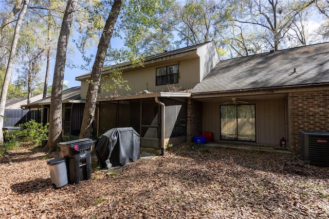 rear view of property with a sunroom, central air condition unit, a ceiling fan, brick siding, and roof with shingles