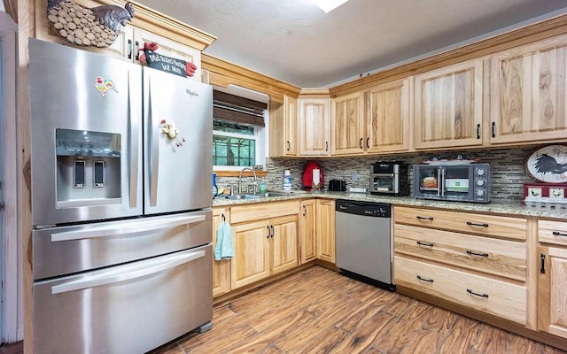 kitchen with light wood-type flooring, light brown cabinets, a sink, appliances with stainless steel finishes, and decorative backsplash