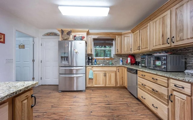 kitchen featuring light stone countertops, wood finished floors, a sink, stainless steel appliances, and backsplash