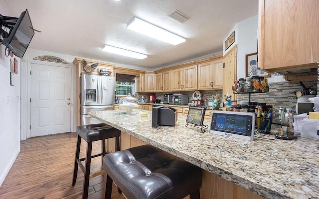 kitchen featuring visible vents, light wood-style flooring, stainless steel refrigerator with ice dispenser, a kitchen breakfast bar, and tasteful backsplash