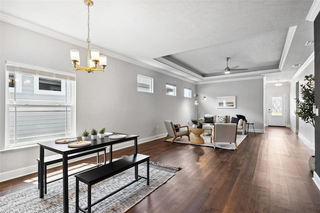 dining room with a tray ceiling, crown molding, dark wood finished floors, baseboards, and ceiling fan with notable chandelier