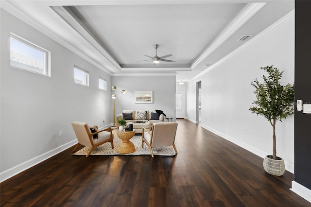 living area featuring a ceiling fan, a tray ceiling, baseboards, and wood finished floors