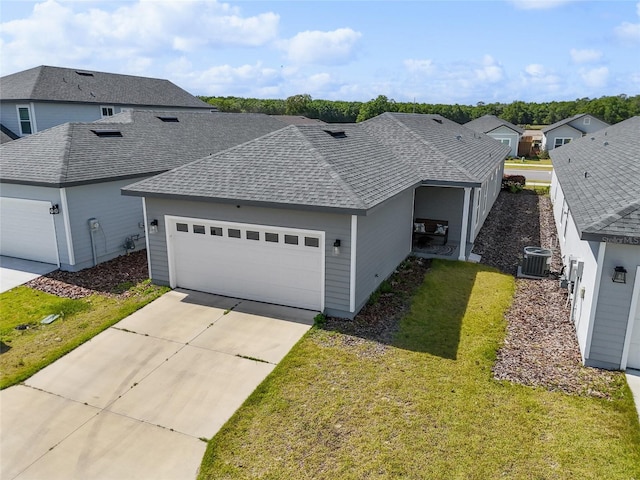 view of front of house featuring an attached garage, central AC, a shingled roof, driveway, and a front yard