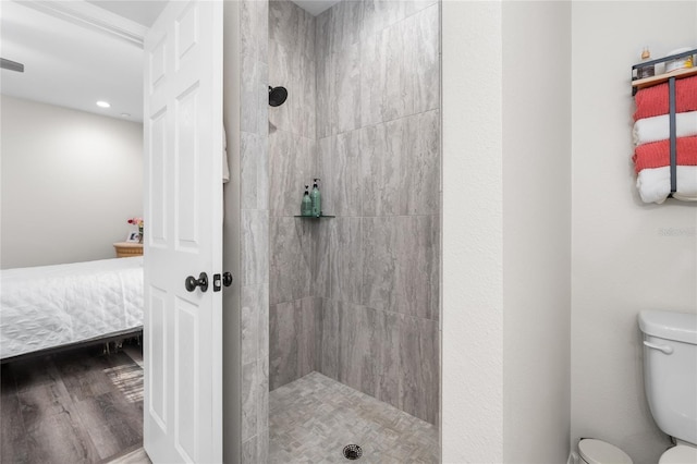 bathroom featuring connected bathroom, tiled shower, toilet, and wood finished floors