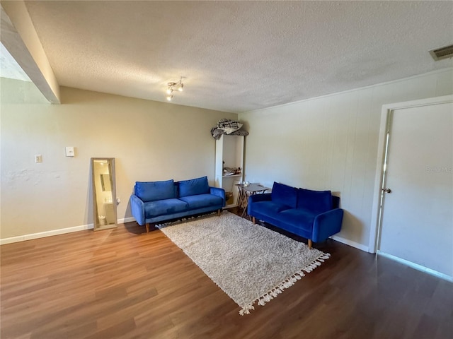 living room with visible vents, baseboards, a textured ceiling, and wood finished floors