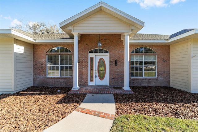 doorway to property featuring brick siding and roof with shingles