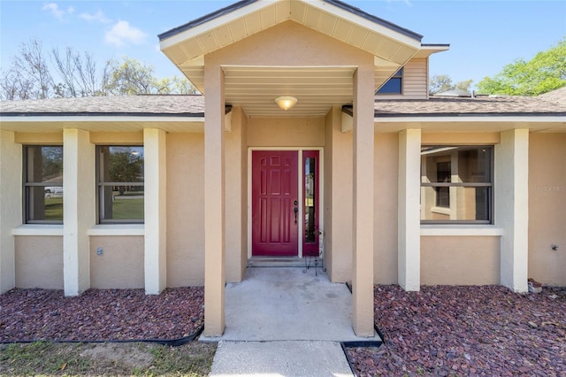 doorway to property featuring roof with shingles and stucco siding