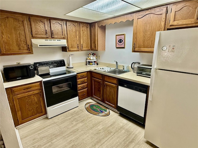 kitchen featuring white appliances, range hood, a sink, light countertops, and light wood-type flooring