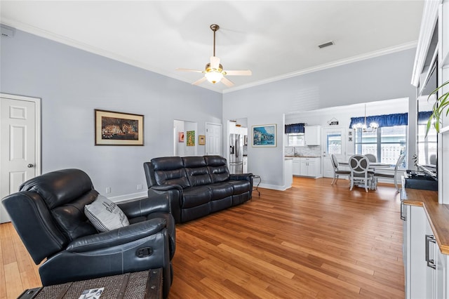 living room with light wood-style floors, ceiling fan with notable chandelier, visible vents, and ornamental molding