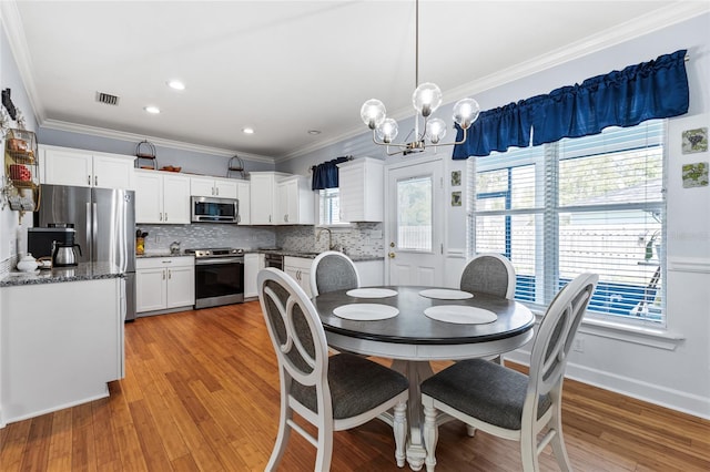 dining room with a healthy amount of sunlight, light wood finished floors, visible vents, and crown molding