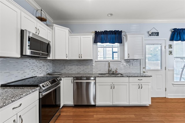 kitchen with crown molding, appliances with stainless steel finishes, white cabinetry, a sink, and wood finished floors