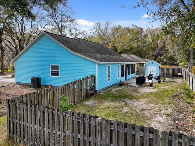 rear view of house with cooling unit, a fenced backyard, and a lawn