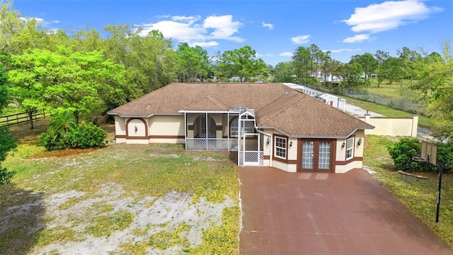 view of front facade with driveway, a shingled roof, a sunroom, fence, and french doors