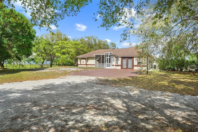 view of front of property with driveway, a patio, a sunroom, fence, and french doors