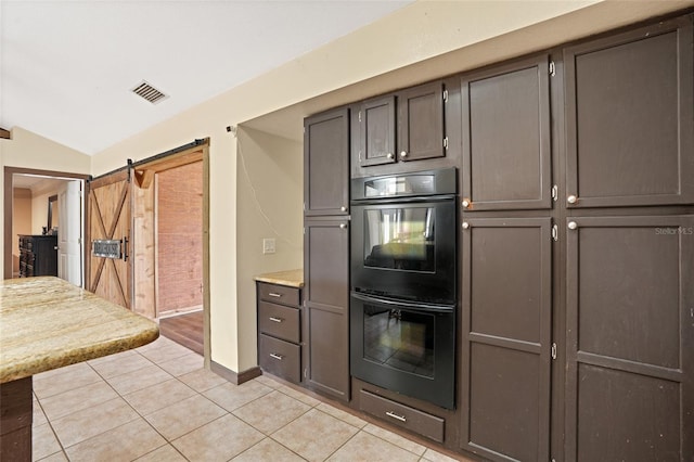 kitchen featuring light tile patterned floors, a barn door, dobule oven black, visible vents, and light countertops