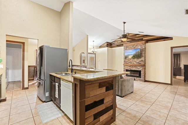 kitchen with open floor plan, light tile patterned flooring, a sink, a stone fireplace, and dishwasher